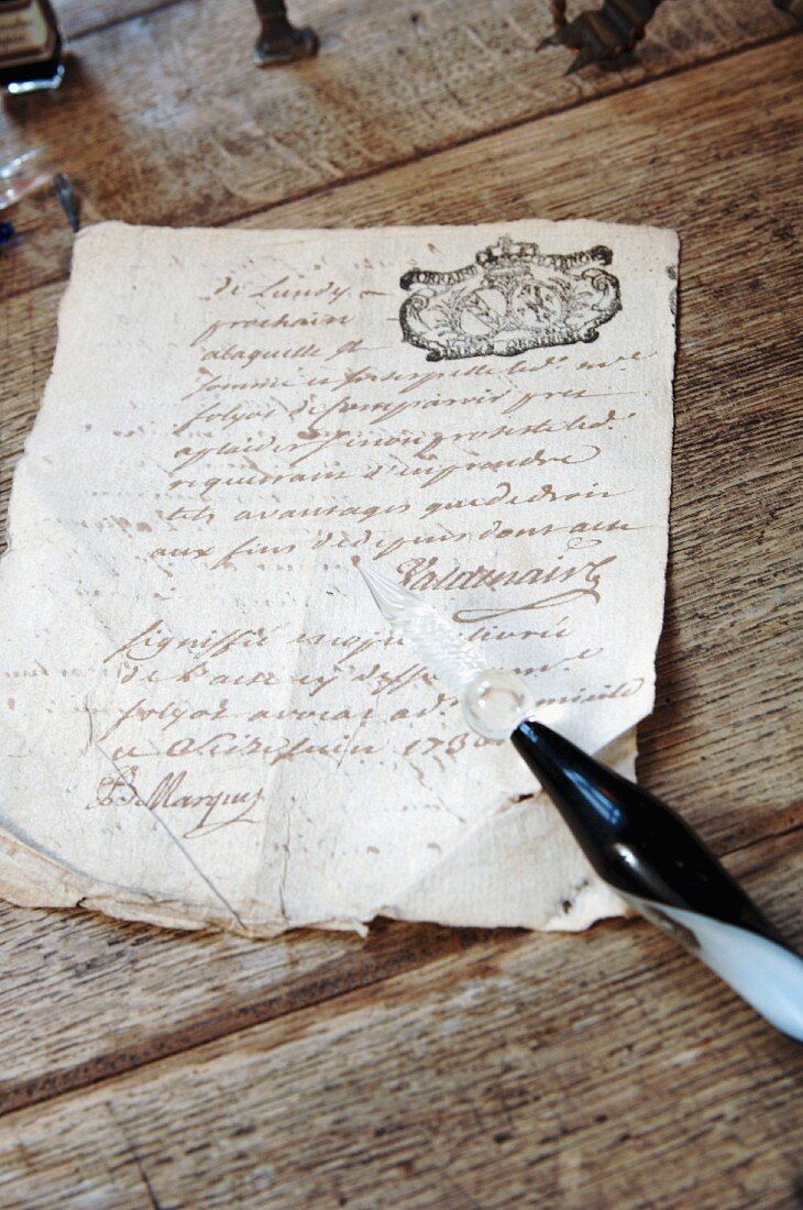 Old, crumpled document and glass quill pen on antique, natural wood table
