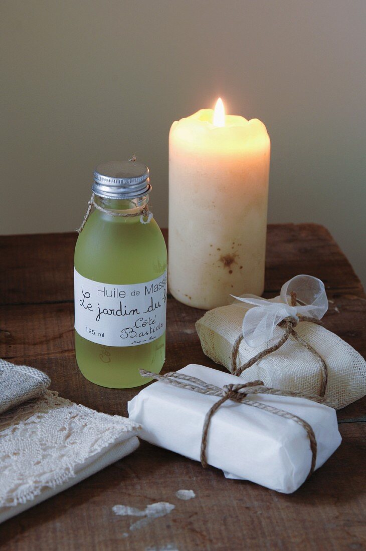 Small bottle of massage oil with label written in French and packaged soaps next to lit candle