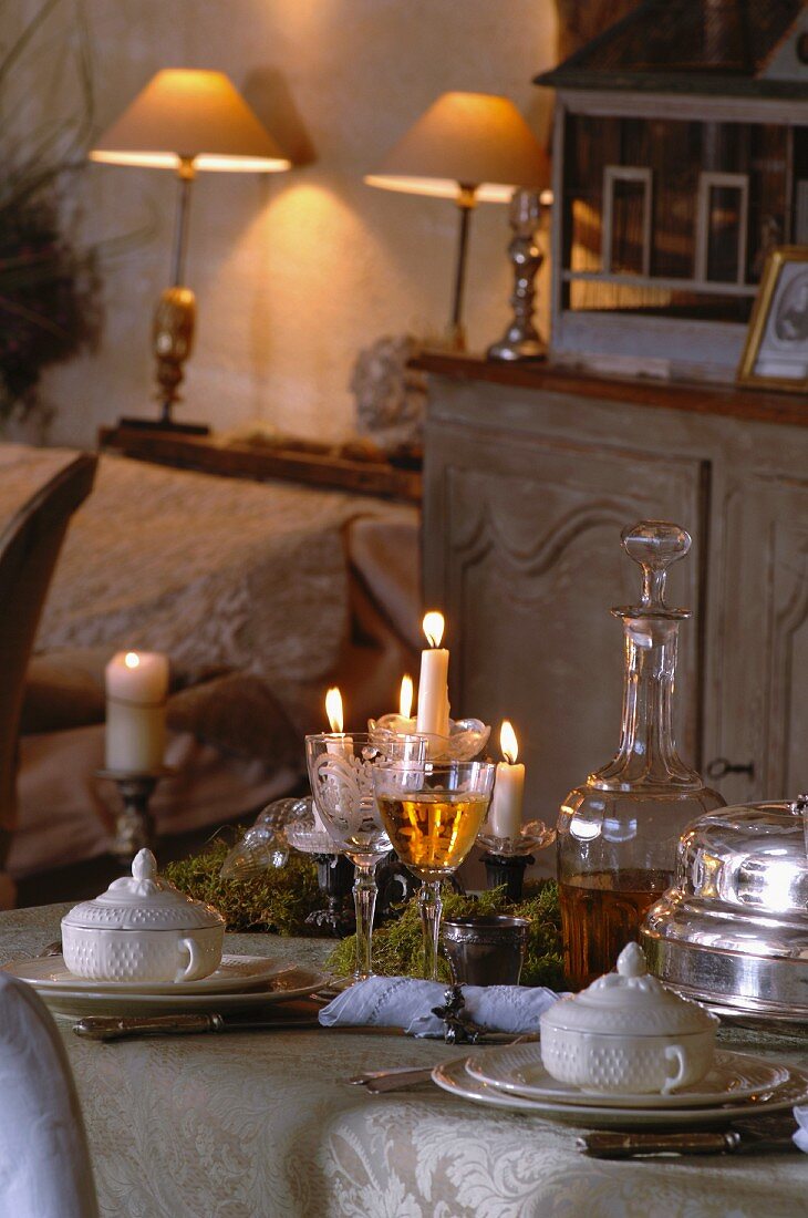 Festlich gedeckter Tisch mit Kerzenlichtstimmung und Tischlampen auf Ablage im Hintergrund