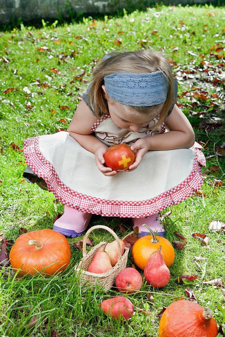 Blondes Mädchen mit Schweizer Apfel, Birnen und Kürbissen im Garten