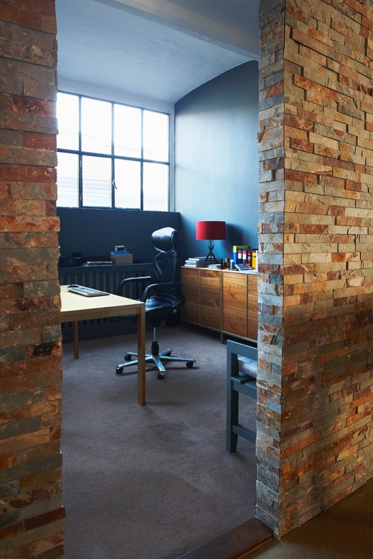 Stone-clad partition wall of loft studio apartment with view of desk and office chair beyond