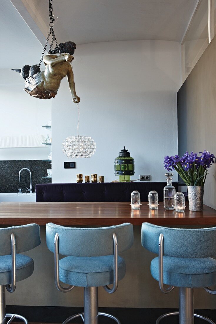 An der Decke hängende Sagengestalt und Theke mit hellblau gepolsterten Barhockern in offener Loftküche