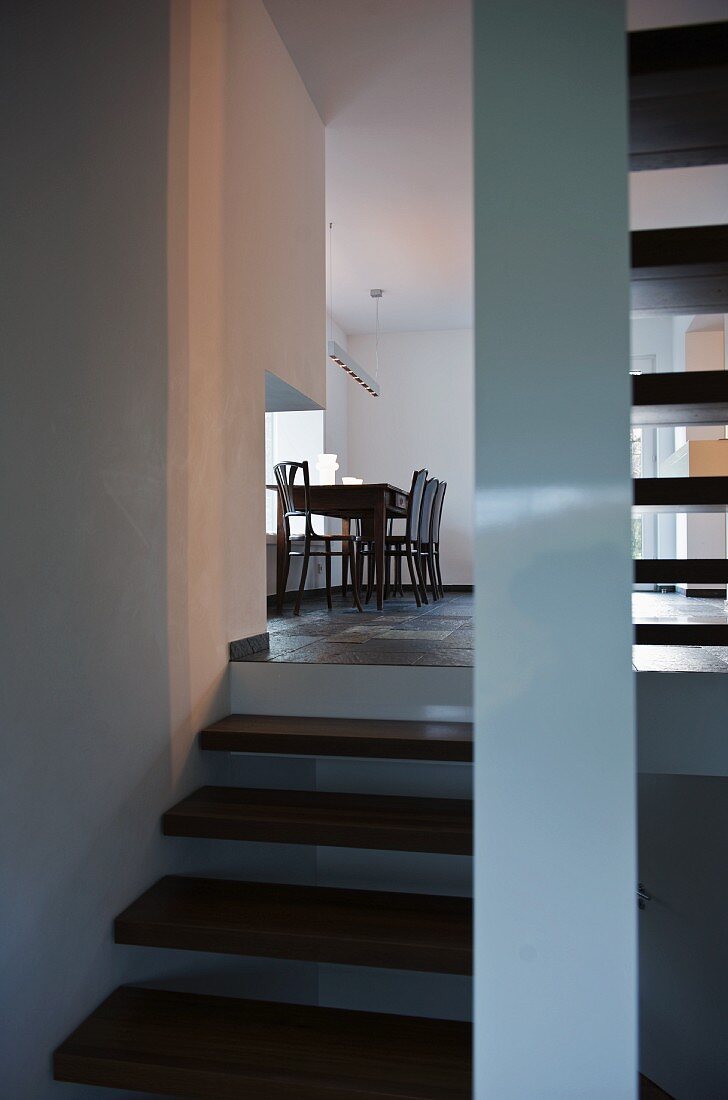 Blick von der Treppe auf den schlichten Esstisch mit Stühlen unter Pendelleuchte am Fenster