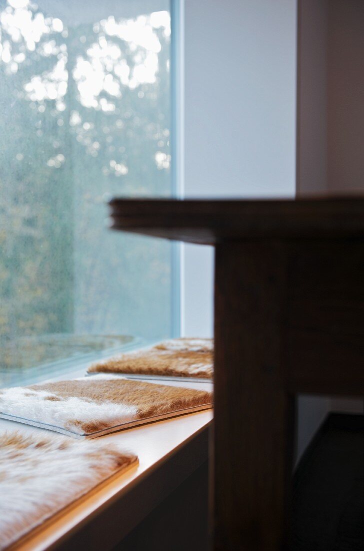 Fellkissen auf der Sitzbank vor dem festverglasten Fensterelement