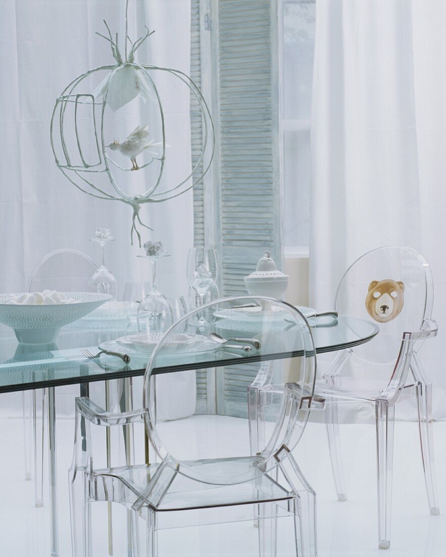 Glasnost in modernem Wohnraum - transparente Kunststoffstühle vor Glastisch und luftiger Vorhang an Fenstertüren