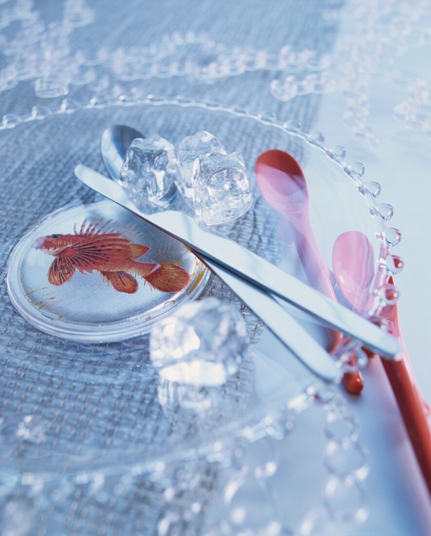 Messer und Löffel auf Kuchenplatte aus Glas mit Fischmotiv und rote Kaffeelöffel