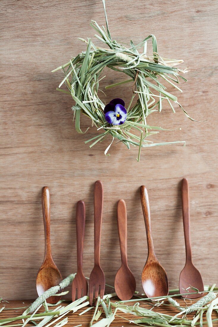 Wooden spoons and hay wreath with one viola flower hanging on wooden wall