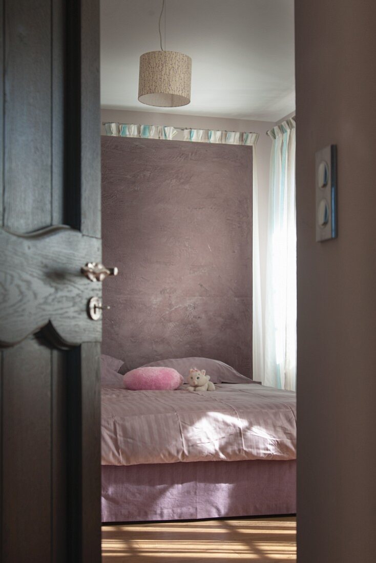 Blick durch halboffene Tür auf Doppelbett vor Raumteiler in pastellfarbenem Schlafzimmer