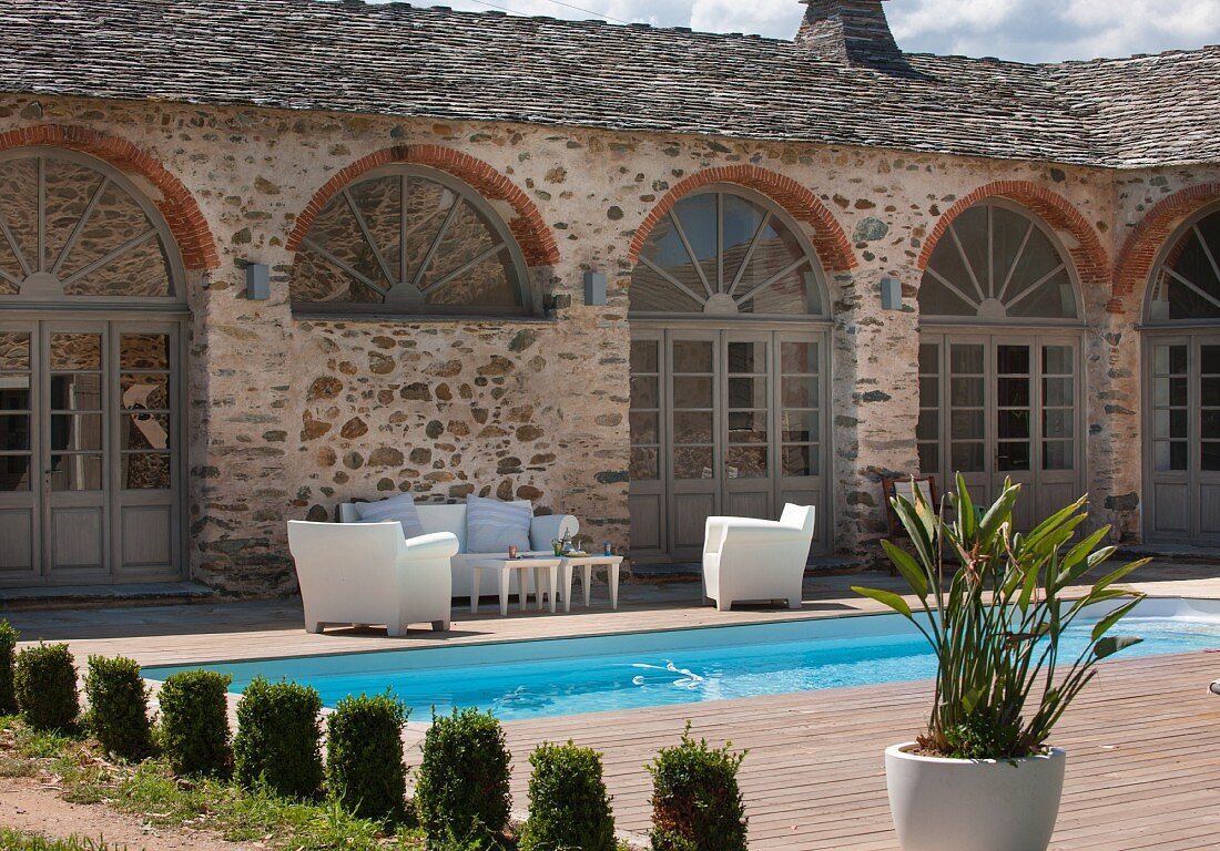 Formgeschnittene Zypressen vor Pool und Terrasse mit weisser Sitzgarnitur im Innenhof einer mediterranen Wohnanlage