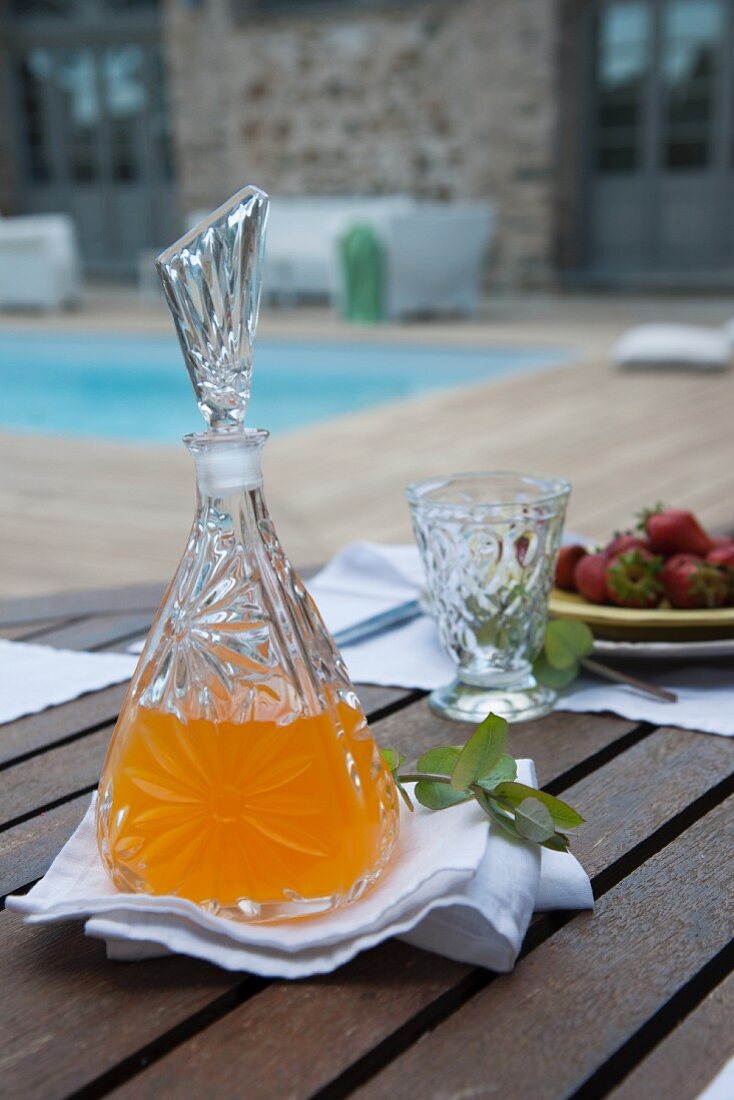 Gedeckter Terrassentisch - Erfrischungsgetränk in Kristallglaskaraffe und Glas auf weisser Stoffserviette