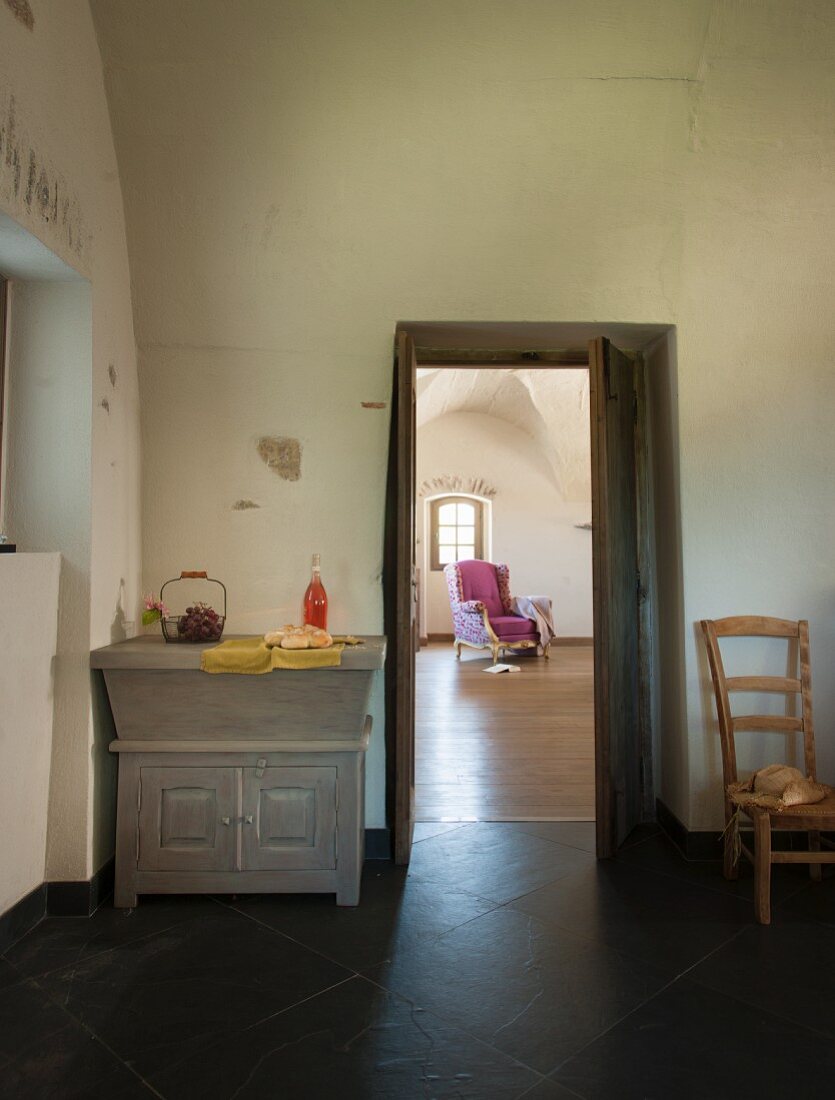 Schlichtes Esszimmer mit rustikaler Kommode neben offener Tür und Blick auf Sessel