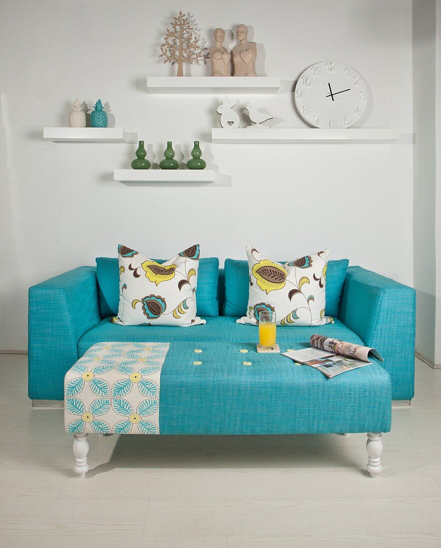 weiße Regale mit Dekoobjekten über einer türkisfarbenen Couch mit Polsterbank