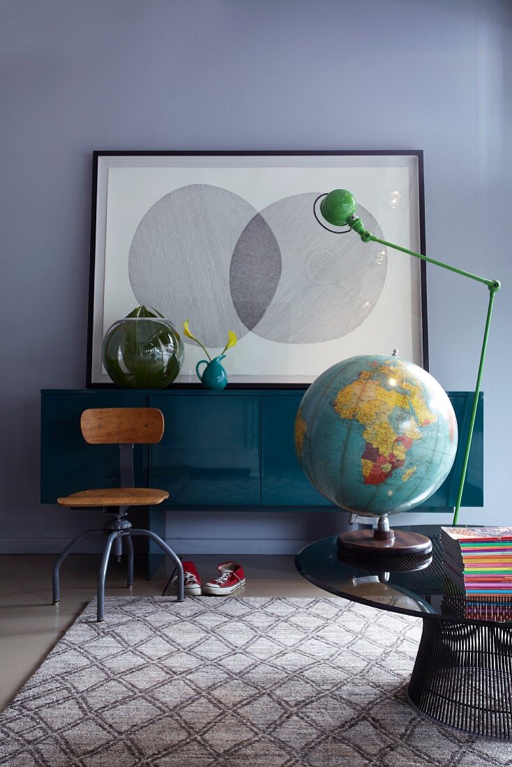 Runder Couchtisch mit Globus und Tischlampe, alter Drehstuhl und Sideboard in einem Zimmer