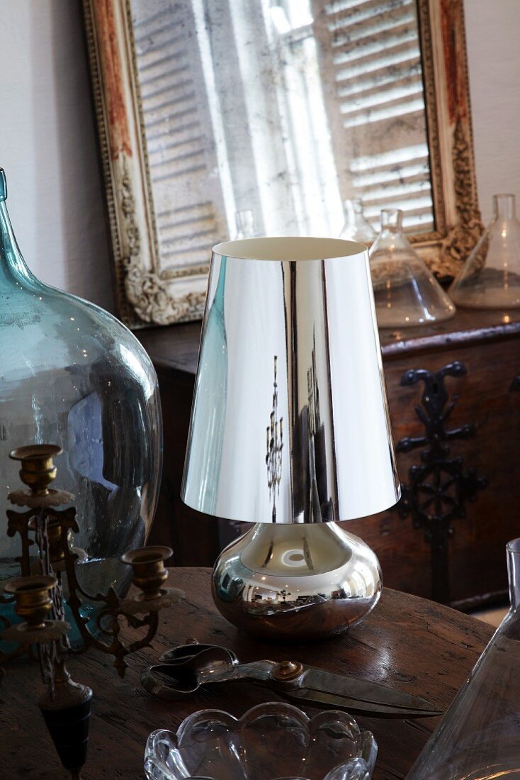 Vintage Kerzenständer, Gartenschere, silberne Tischlampe und Glasballon auf einem Holztisch