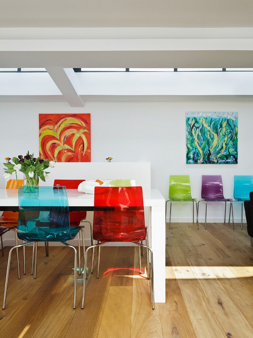 Colourful plastic chairs at white dining table opposite modern artworks on wall