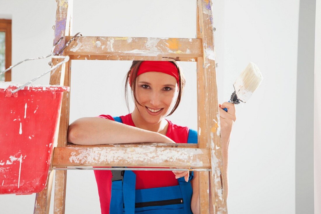 Woman holding paint brush leaning on ladder