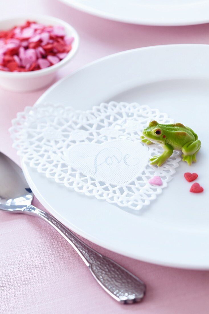 Place setting decorated with doily, frog ornament & sugar hearts