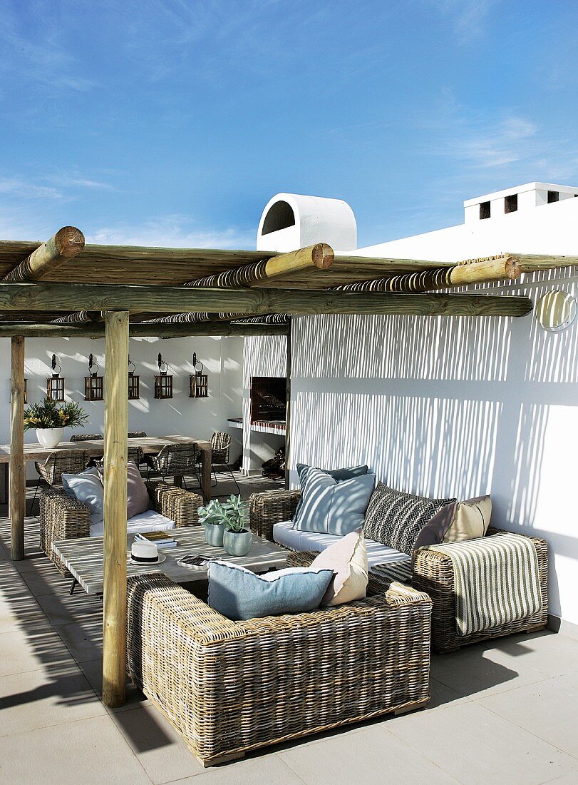 Mediterranean holiday home with rattan furniture below pergola on terrace