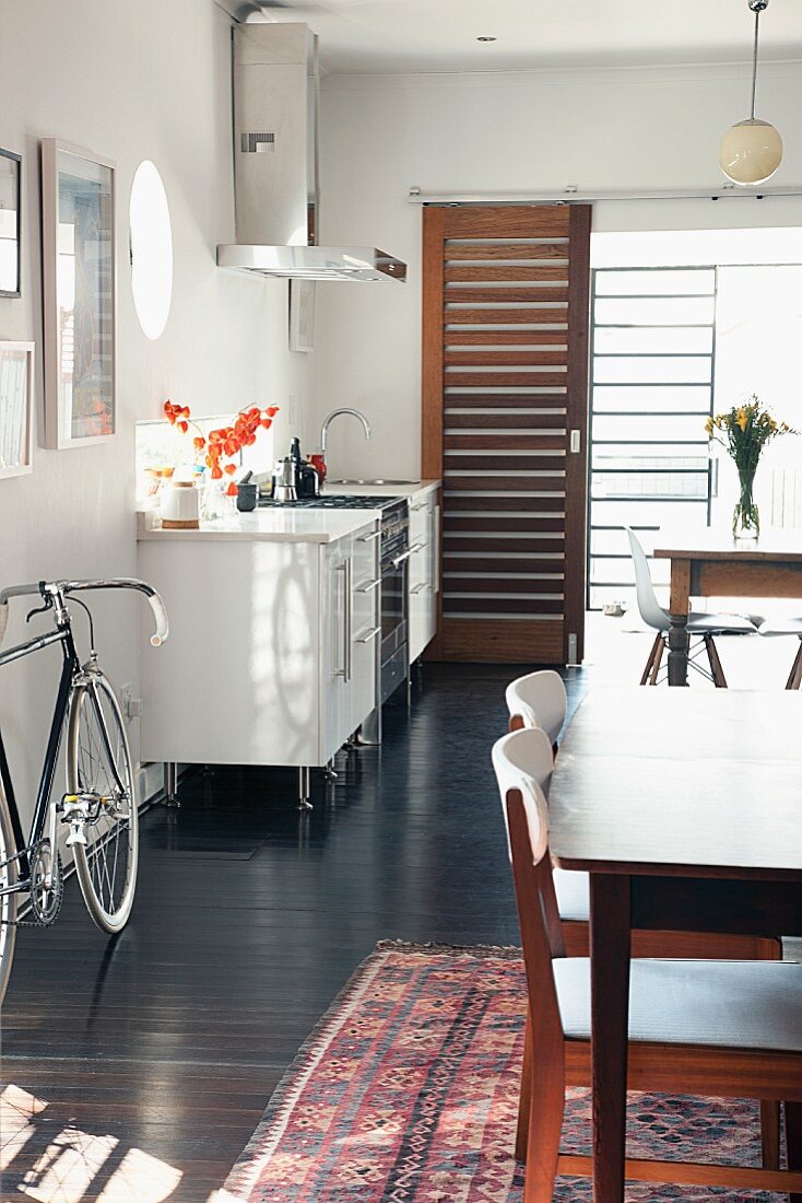 Small kitchen counter, two dining tables and racing bicycle in open-plan interior