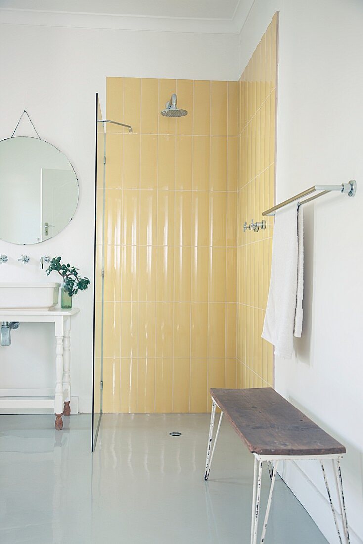 Pastellgelbe Retrofliesen in bodengleicher Dusche mit Glasabtrennung und Vintage Ablagebank