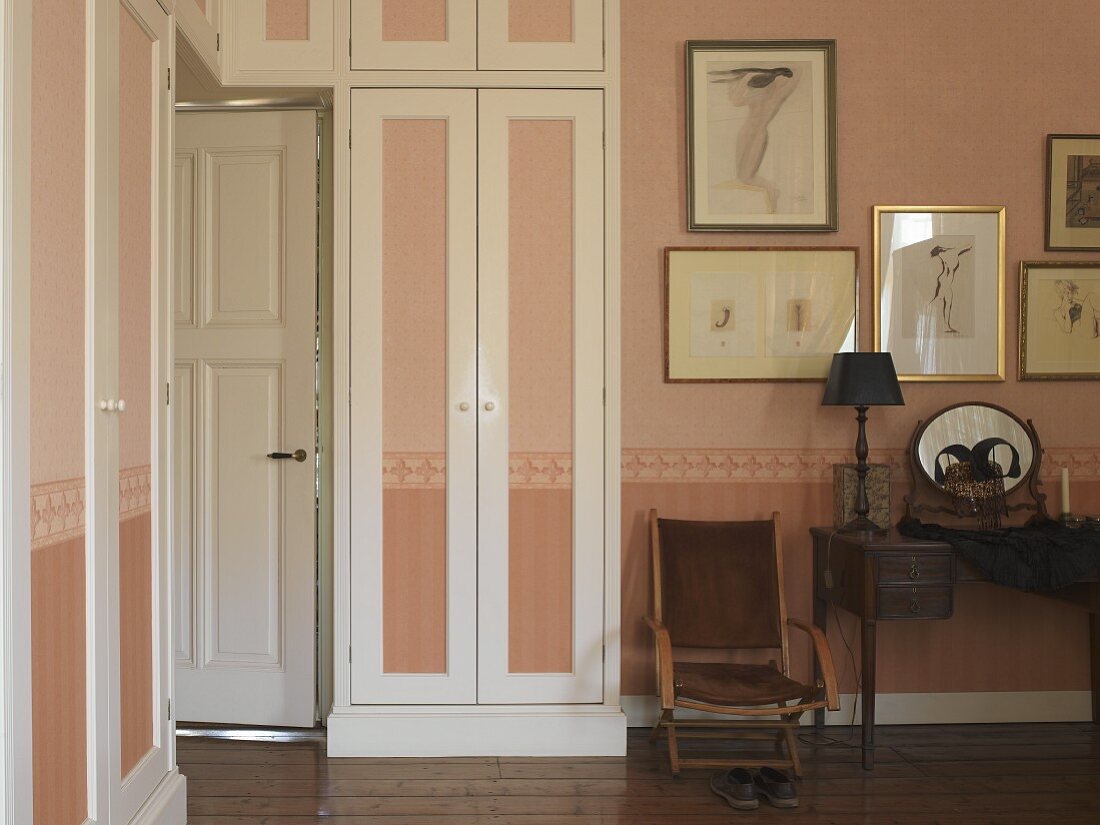 Interior door surrounded by fitted wardrobes in stylish bedroom; walls and wardrobe doors in pastel pink with continuous border