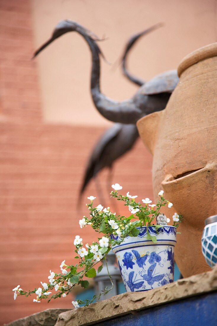 Potted plants with white flowers on step in front of terracotta pot and ornamental crane figures