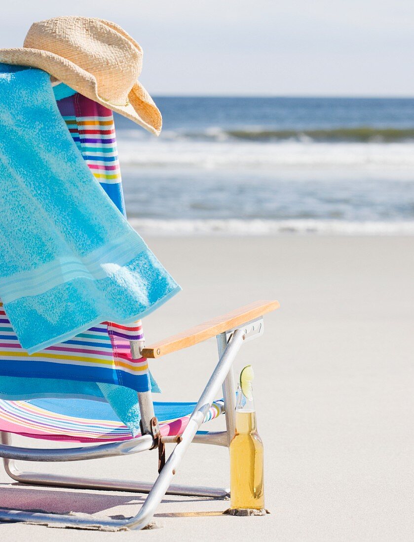 Eine Flasche Bier neben einem Strandstuhl mit Handtuch und Hut