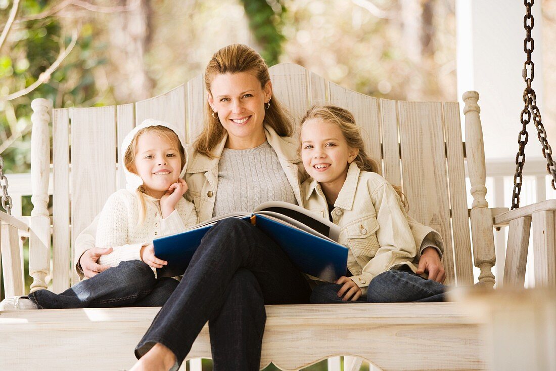 Mutter mit Töchtern beim Vorlesen auf der Schaukel