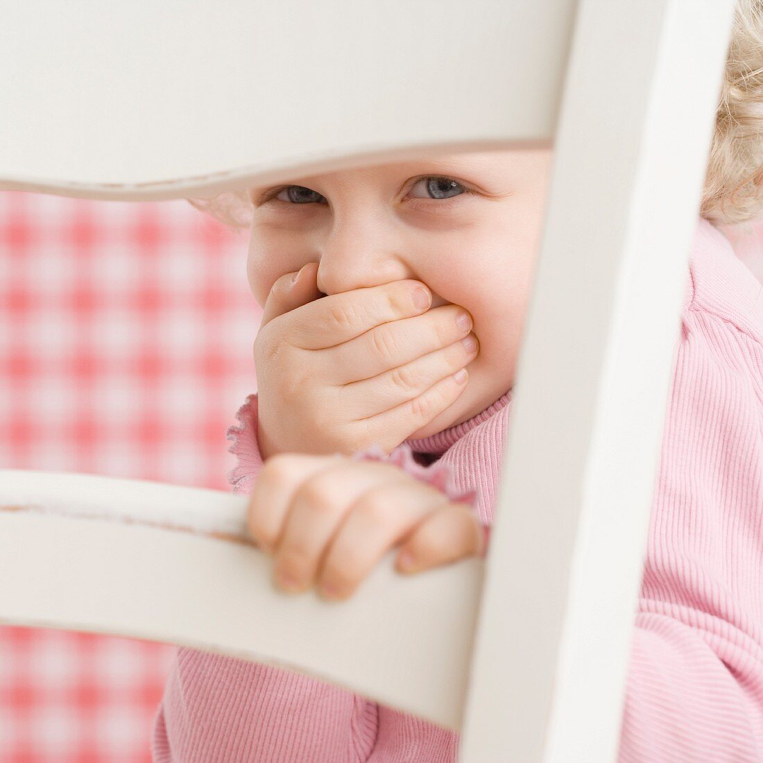 Kleines Mädchen versteckt sich hinter einem Stuhl