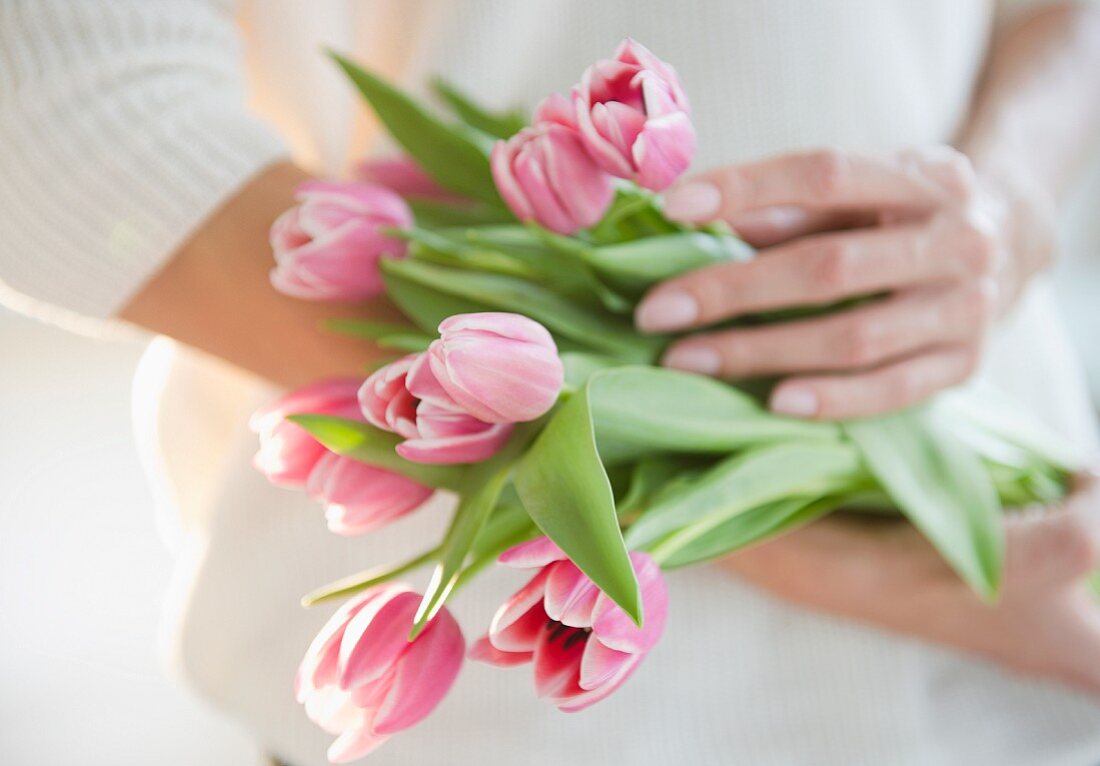 Frau hält Blumenstrauss mit rosafarbenen Tulpen