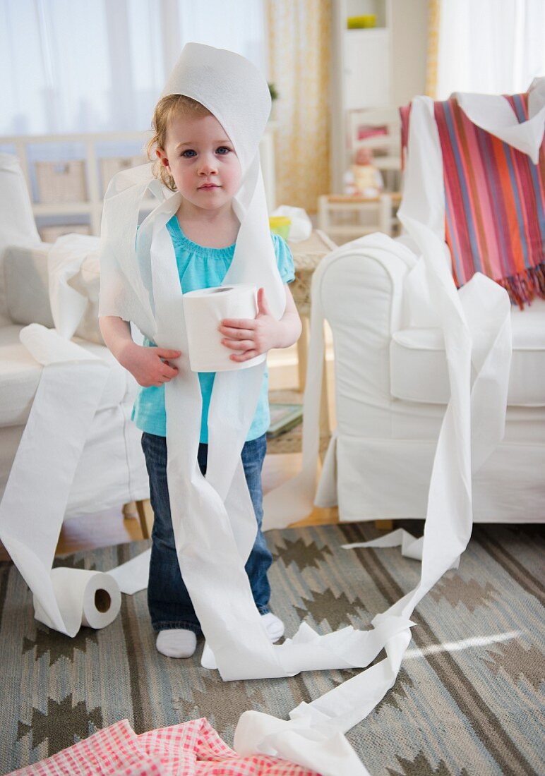 Girl (2-3) wrapped with toilet paper standing in living room