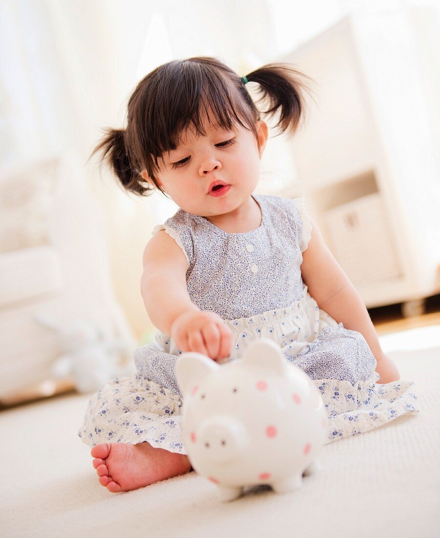 Baby girl (12-17 months) playing with piggy bank