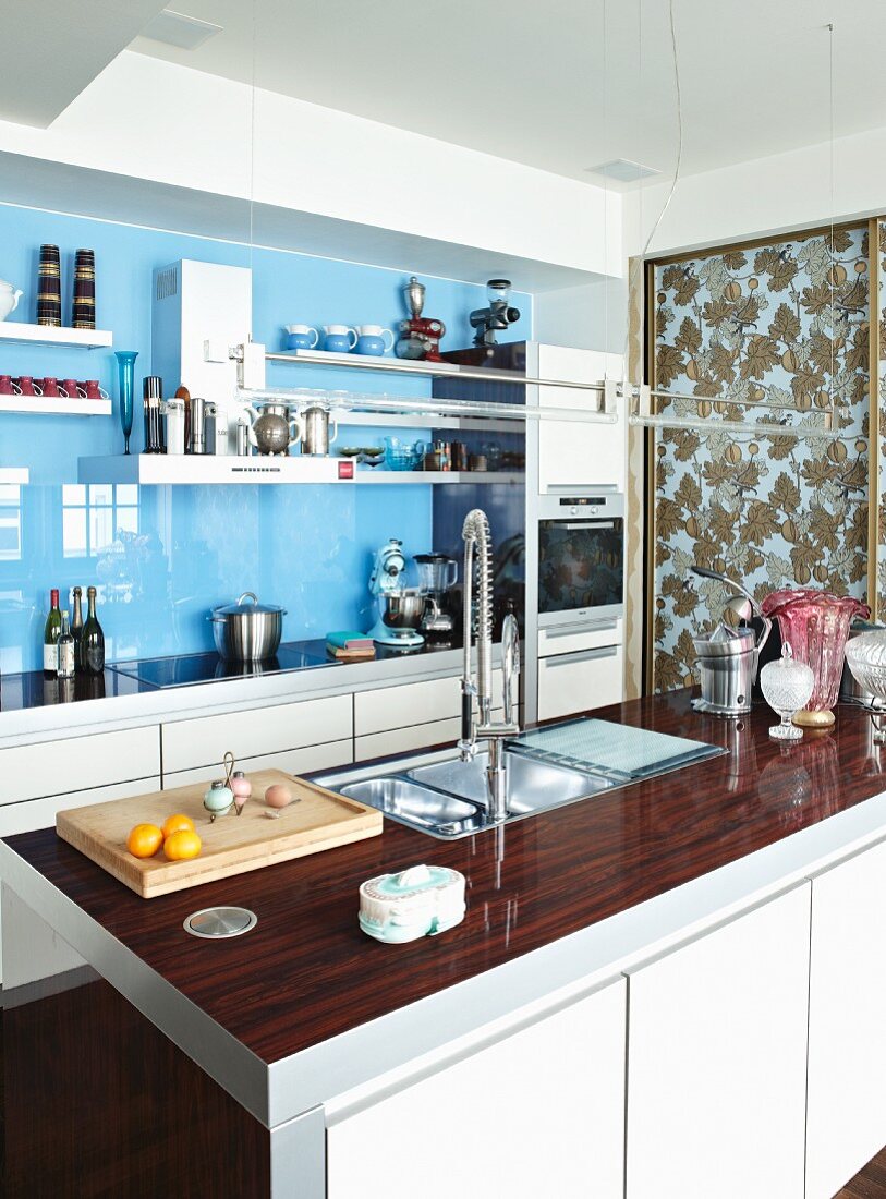 Modern kitchen with glossy splashback and white cupboard doors; sliding door with pattern of autumnal leaves in background