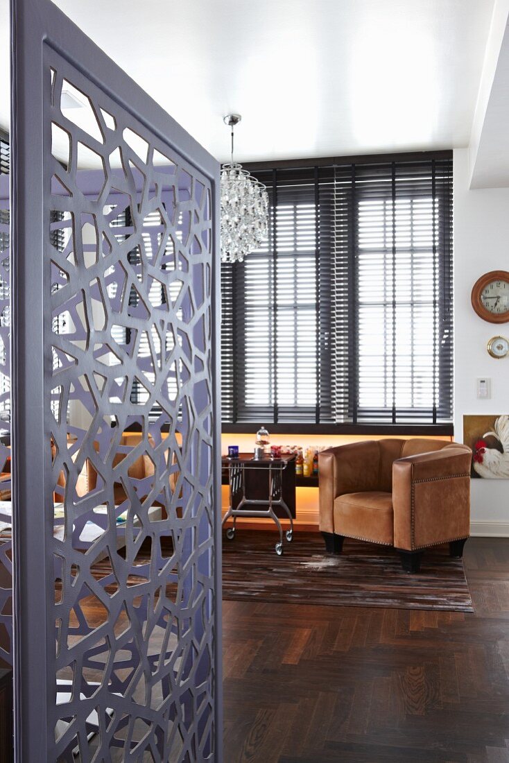 View into office with grey, metal screen; dark, exotic wood parquet floor and brown leather armchairs