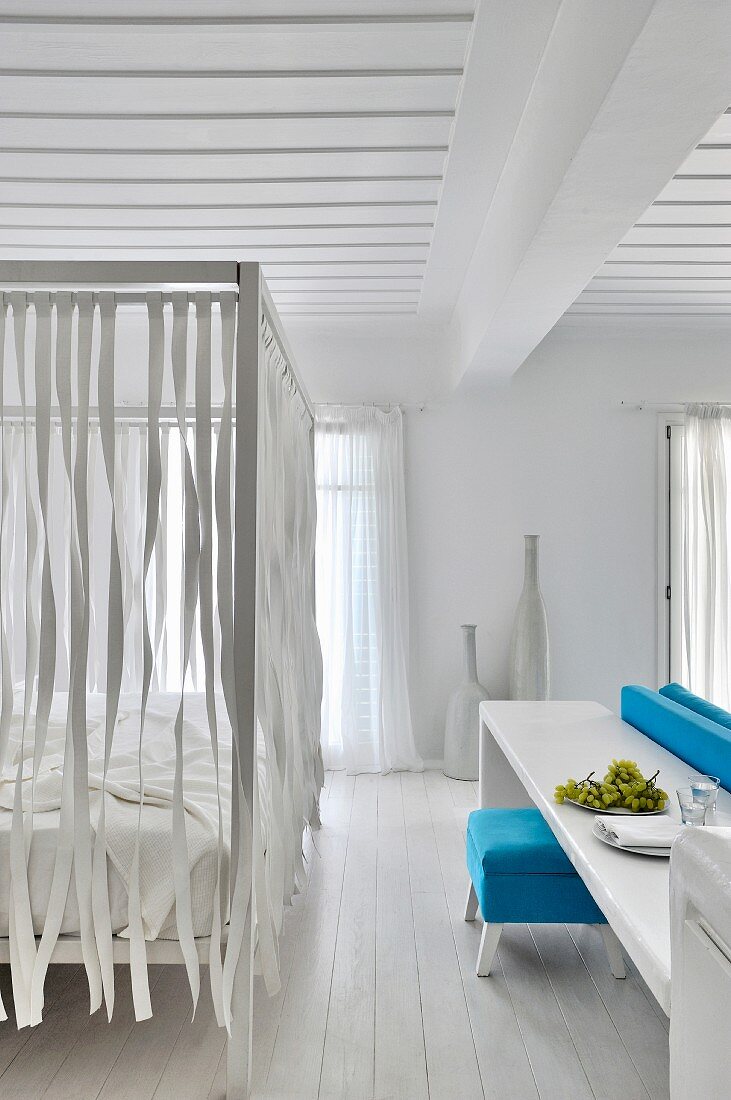 Himmelbett mit aufgehängten Bändern in weißem Schlafzimmer mit Holzdecke und mediterranem Flair