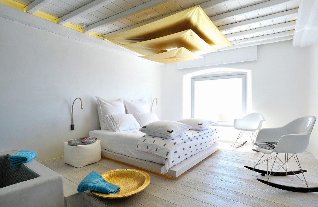 Hängeleuchte aus goldfarbenen, übereinander gehängten Segeln in mediterranem Schlafzimmer mit Bauhaus Schaukelstühlen vor Doppelbett
