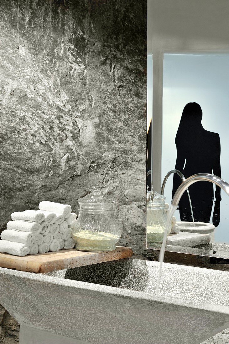 Stone trough and towels on vintage wooden board against stone wall with silhouette motif of woman on glass door