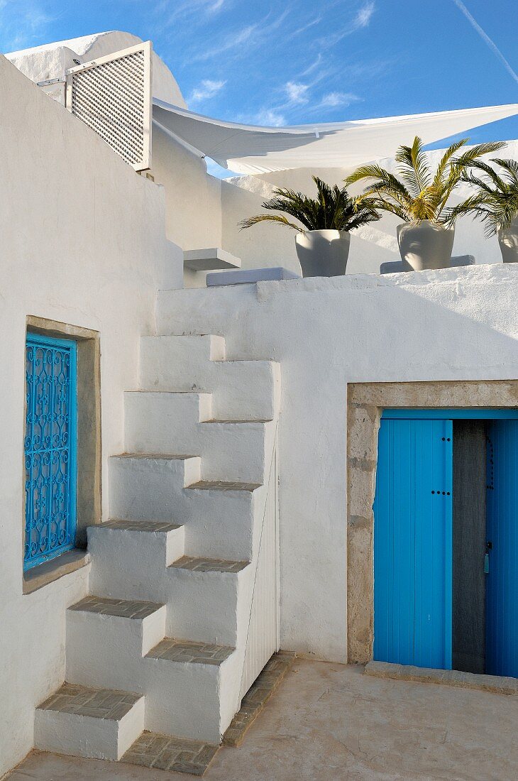 Blaue Tür und Fenstergitter in nordafrikanischem Innenhof mit gemauerter Sambatreppe zur Dachterrasse