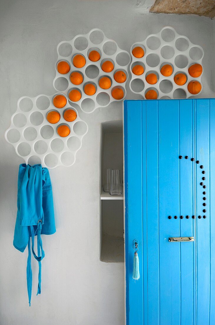 Lochformen an der Wand für dekorative Orangenaufbewahrung; geöffnete Tür und Schürze im gleichen Blau