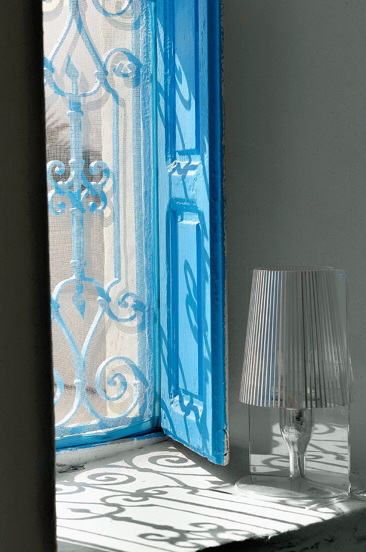 Fensternische mit blauem Holzladen und dem Schattenwurf eines orientalischen Gitters