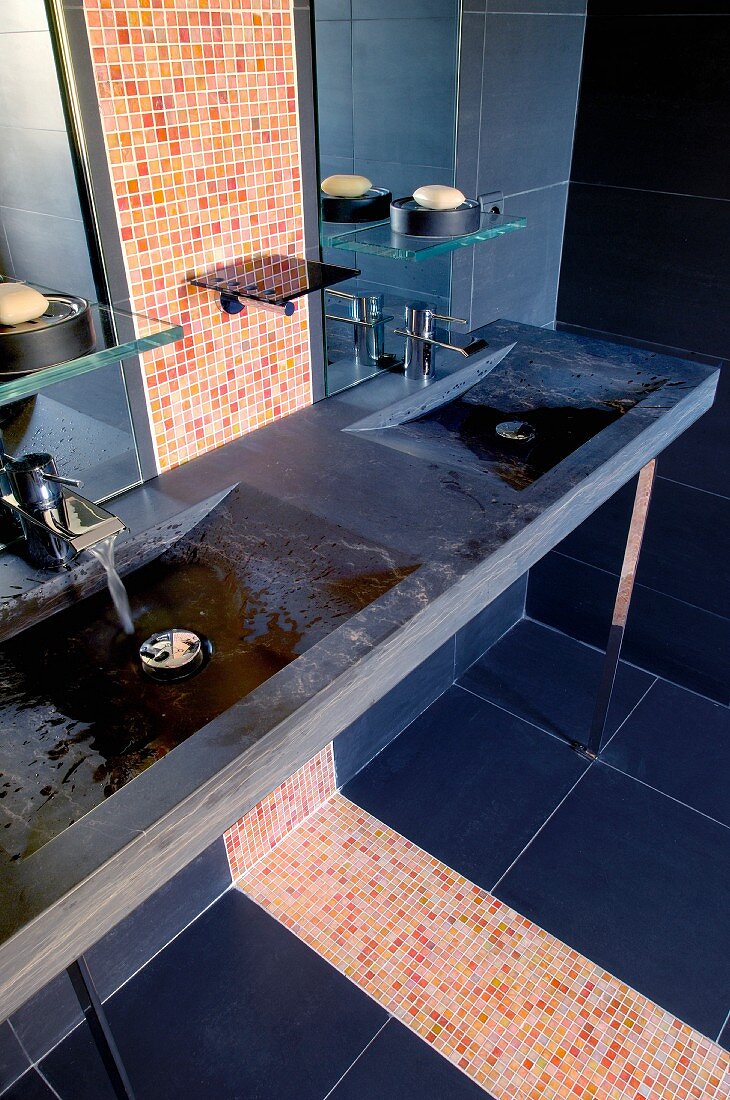 Dunkle Steinplatte mit eingearbeiteten Waschbecken und buntem Mosaikfliesenstreifen in modernem Bad