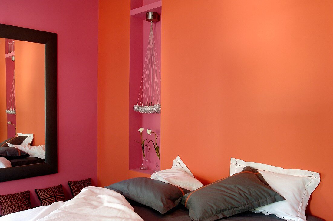 Bett mit braunen und weissen Kissen vor orange getönter Wand in modernem Schlafzimmer
