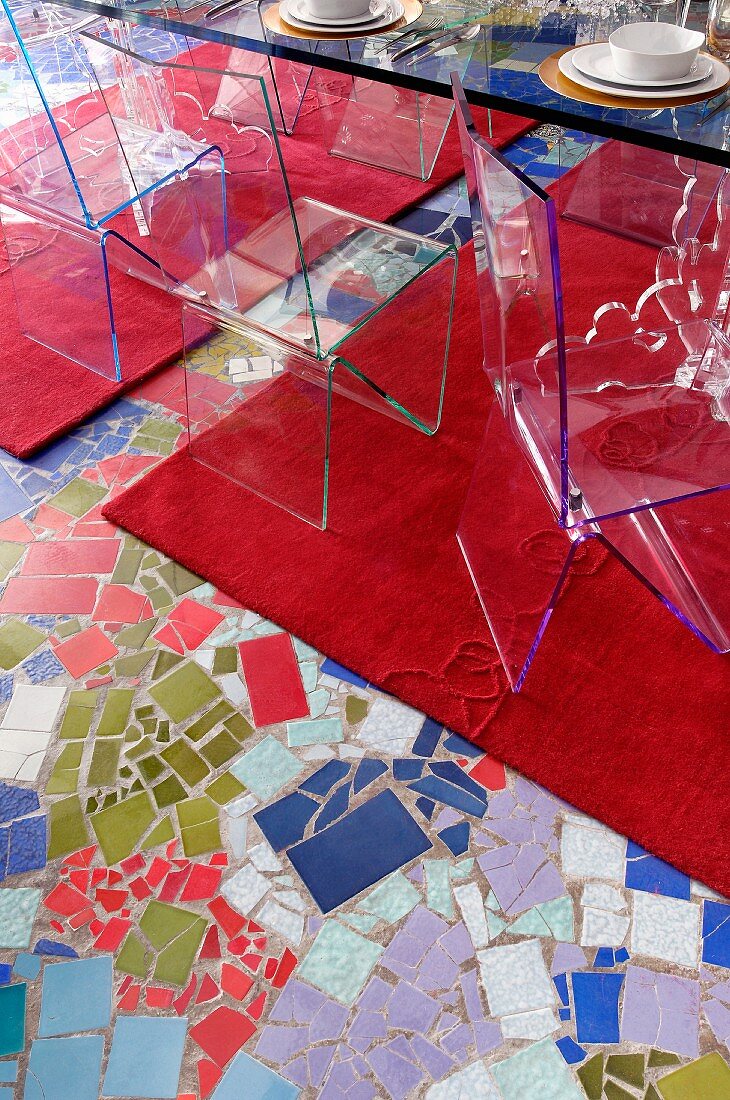 Stühle aus transparentem Kunststoff auf rotem Teppichläufer und mosaikartig gestaltetem Fussboden