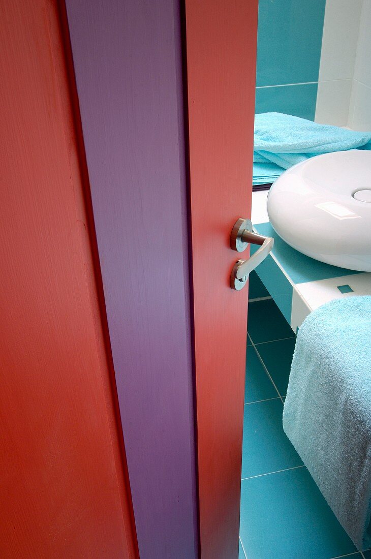View of modern washbasin on tiled counter seen through bathroom door painted red and purple