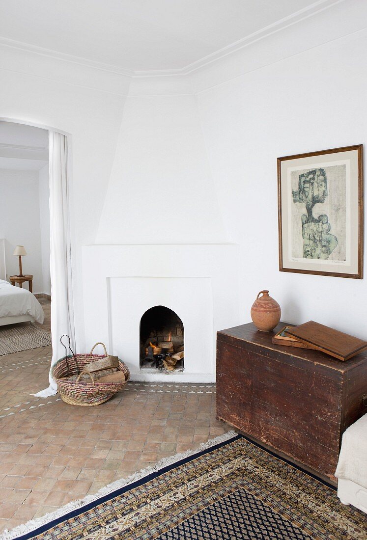 Simple, Moroccan interior with modern painting above old wooden trunk and masonry fireplace in corner