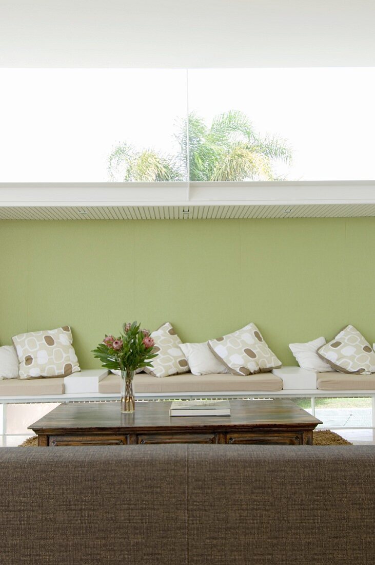 Back of couch in front of table and bench with seat cushions against green-painted wall with long transom window