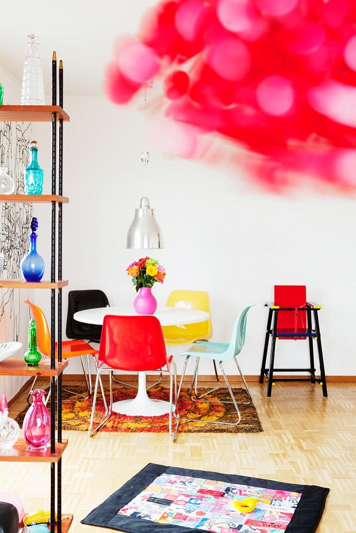 Wohnraum im Retrostil mit rundem Esstisch, bunten Kunsttoffstühlen, Babykrabbeldecke & Kinderhochstuhl