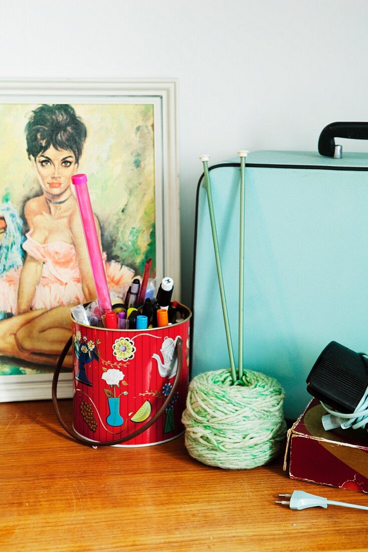 Picture of woman, bag, metal can of pens & knitting yarn on cabinet