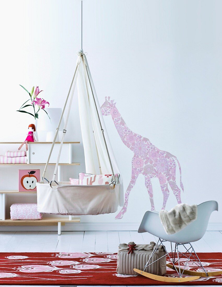 An der Decke aufgehängte Säuglingswiege vor dekoriertem Regal und floraler Wandillustration Giraffe
