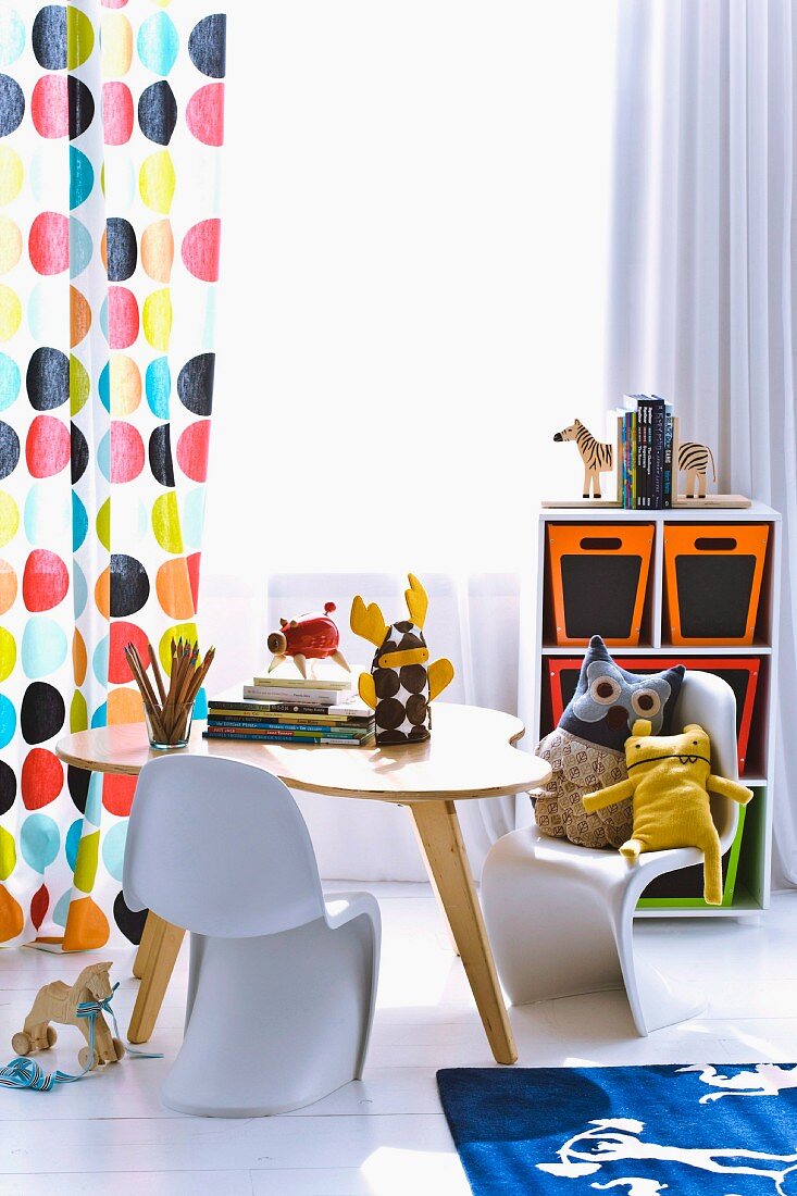 Curtain with pattern of coloured circles, retro table and cuddly toys on child's version of classic Panton chair